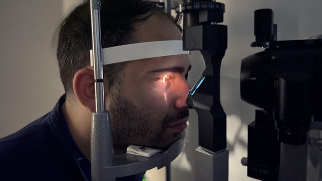 A young adult male patient having light shined into his eye during an eye exam.